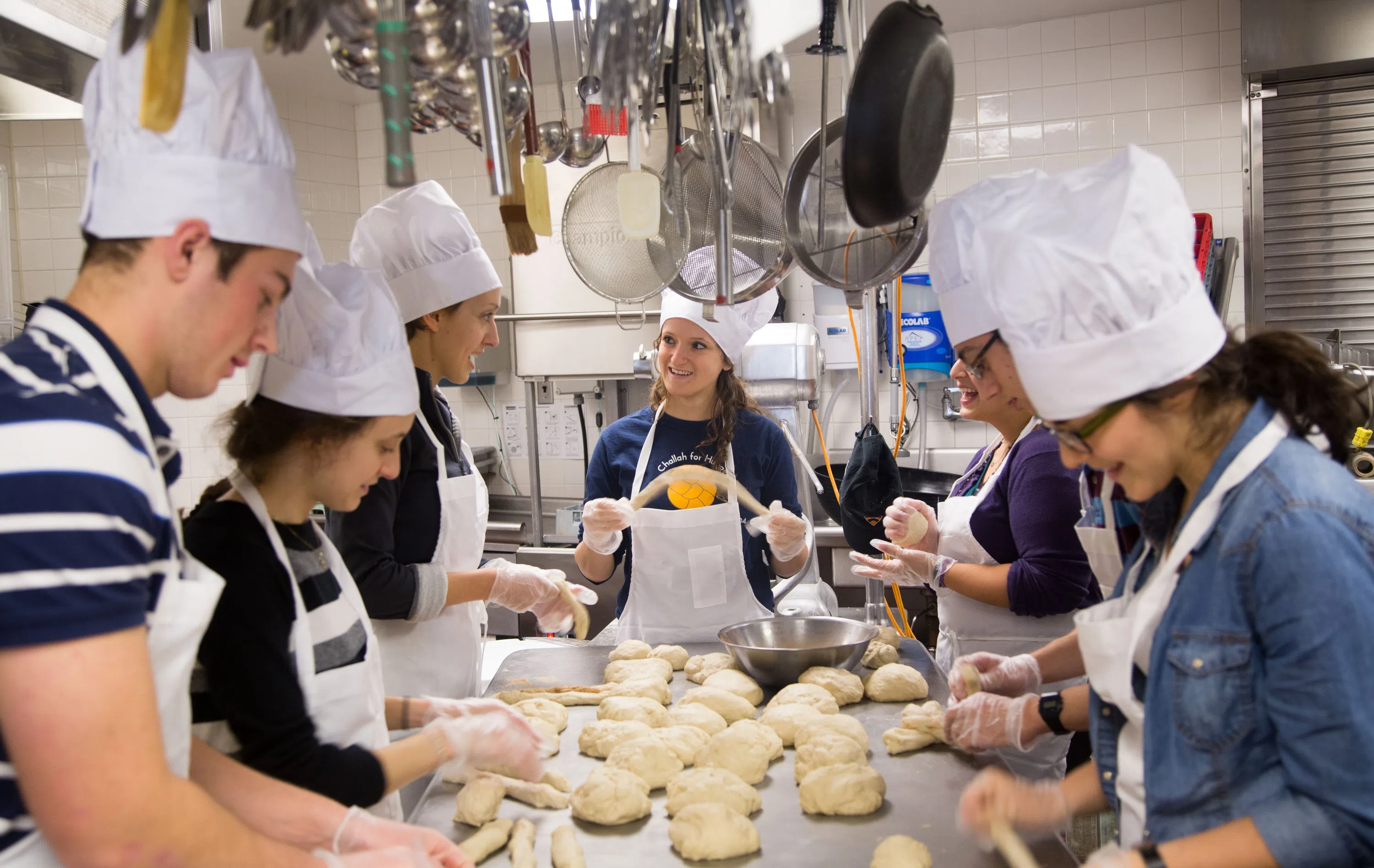Students making braided challah bread in a kitchen 