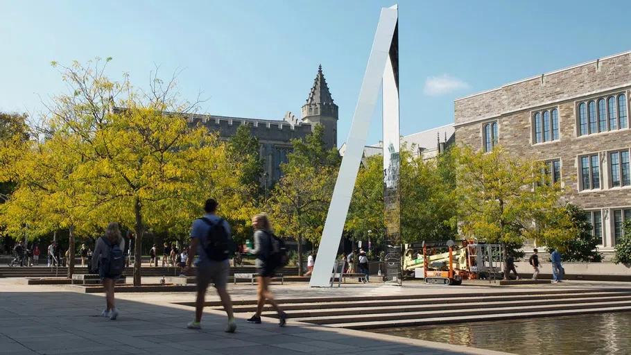 Large installation sculpture in plaza with student walking by. 