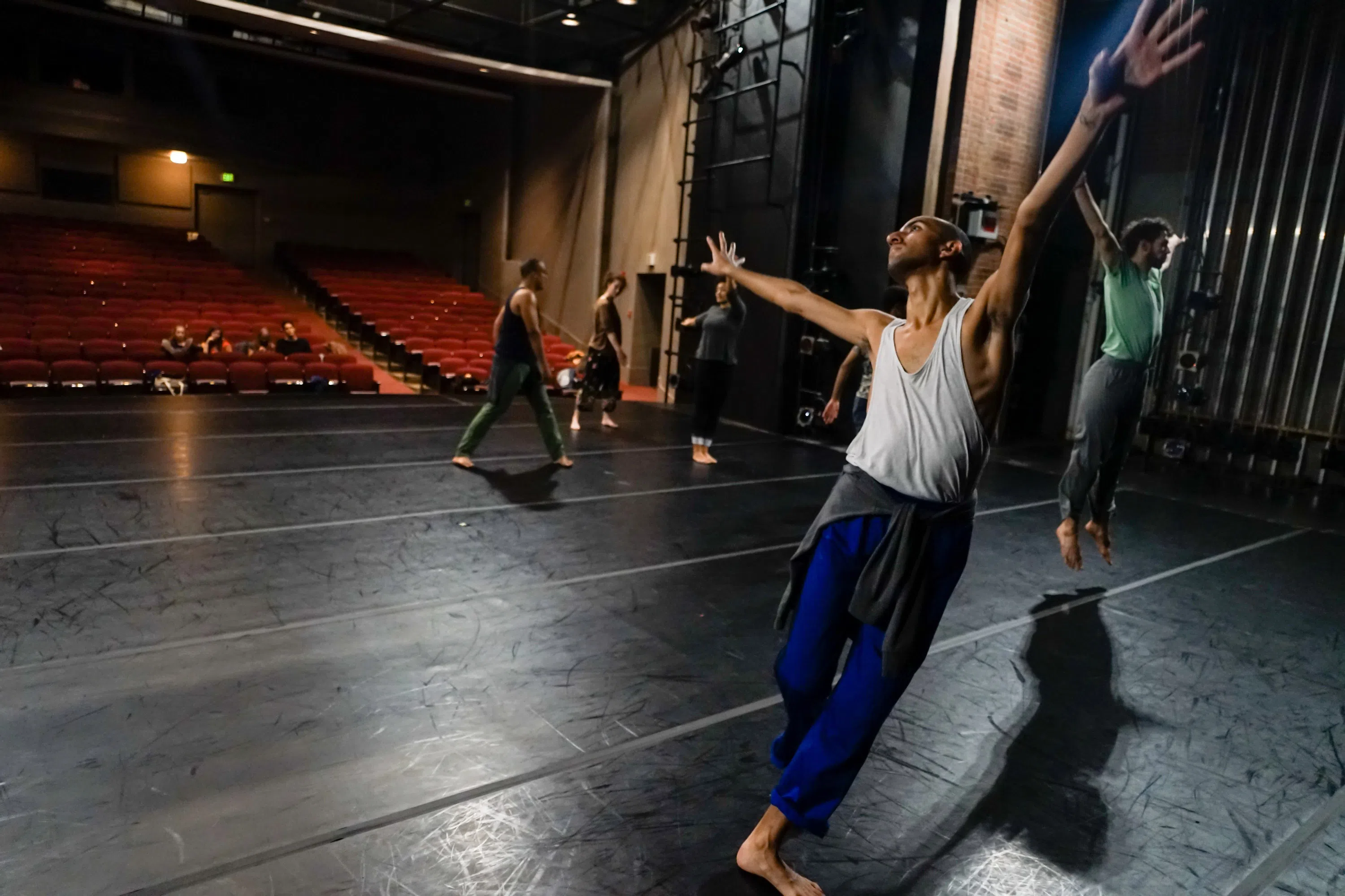 Five dancers practicing on stage with the empty audience seats in the background.