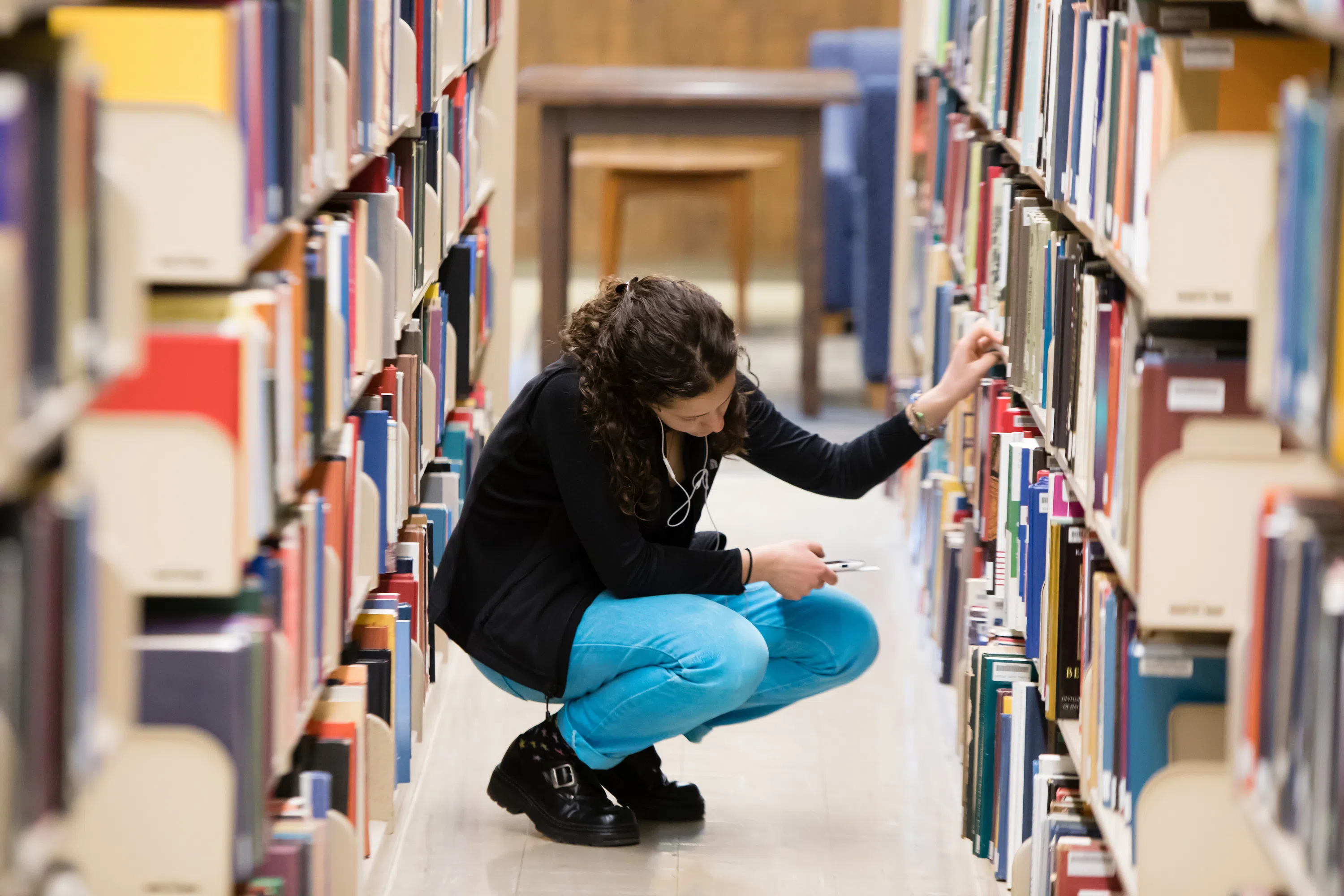 Student squatting down in aisle of book stacks looking for a book.