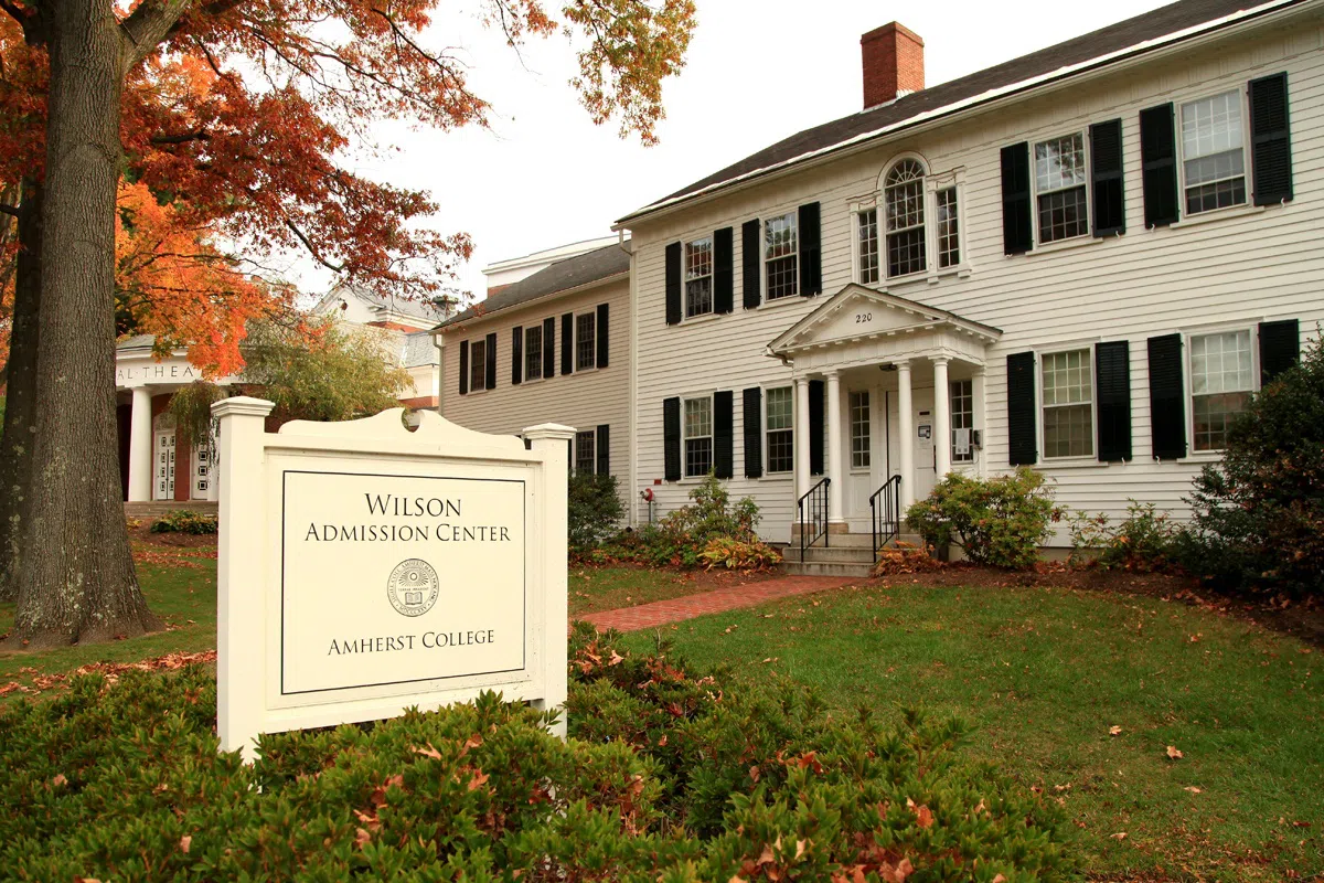 Exterior shot of older white New England building with brick walkway in forefront.