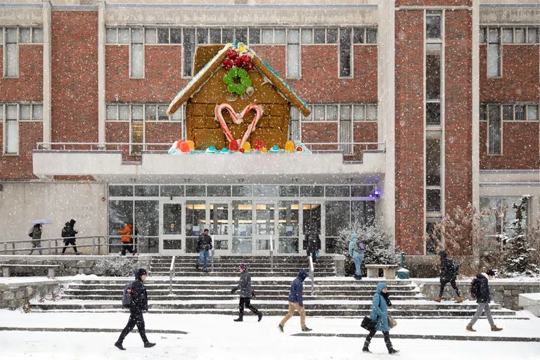 Exterior shot of Frost Library with snow on ground and people walking by. Large decorate gingerbread house on top.