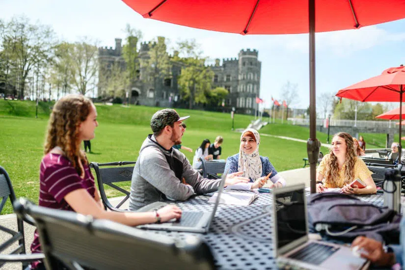 Students enjoy the nice weather at umbrella tables outside of The Commons with The Castle in the background