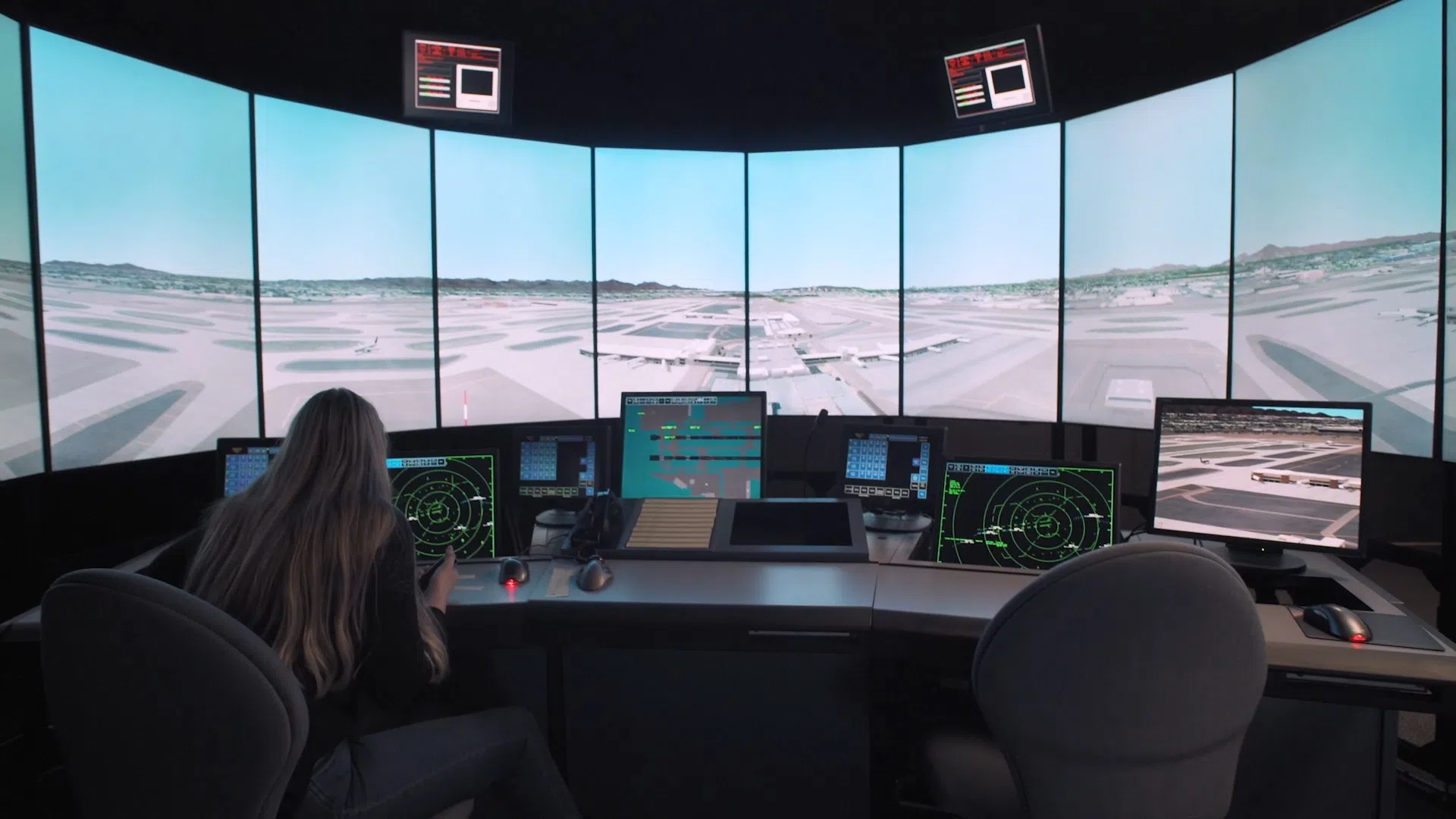 Woman sits at set of computer screens and controls of an air traffic control station simulator.