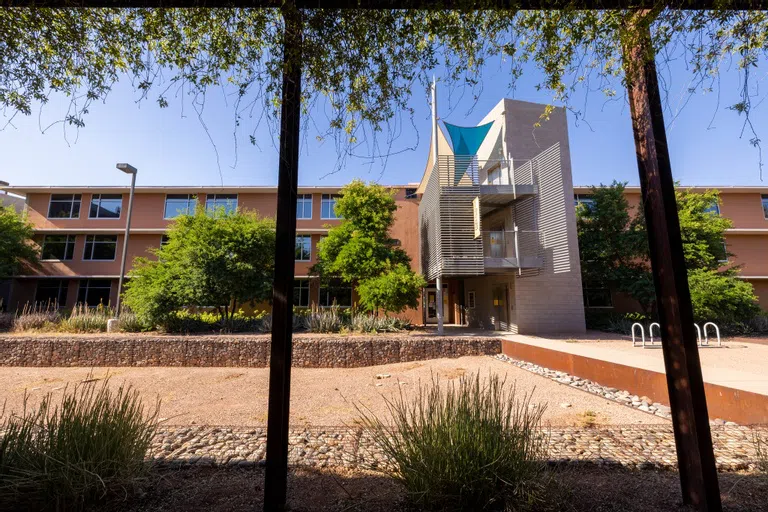 A three-story orange building is framed by a metal structure draped in foliage.