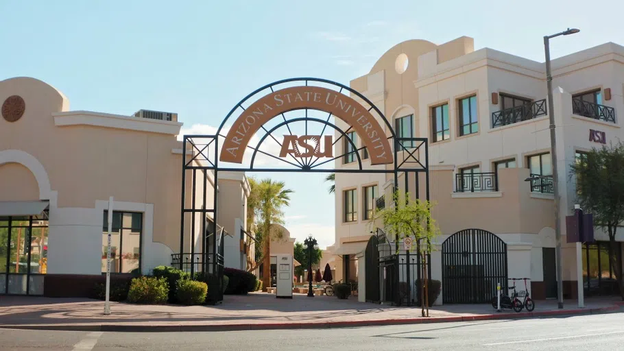 Wrought iron gate with ASU logo on it in front of Spanish mission-style buildings.