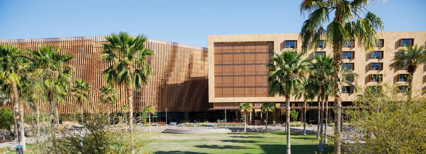 Palm trees and a lawn are in front of a six-story copper colored building.