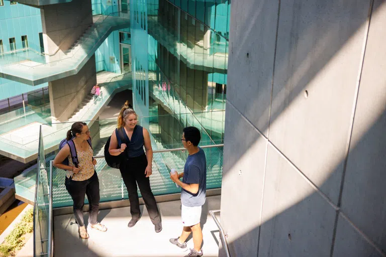 Three people standing on an outdoor stair landing talking to each other.