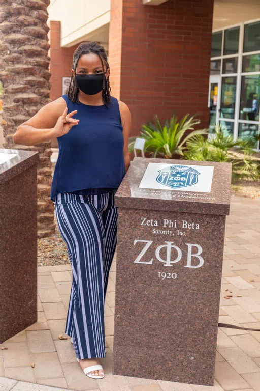 A representative from the Zeta Phi Beta Sorority stands next to her society's plaque.