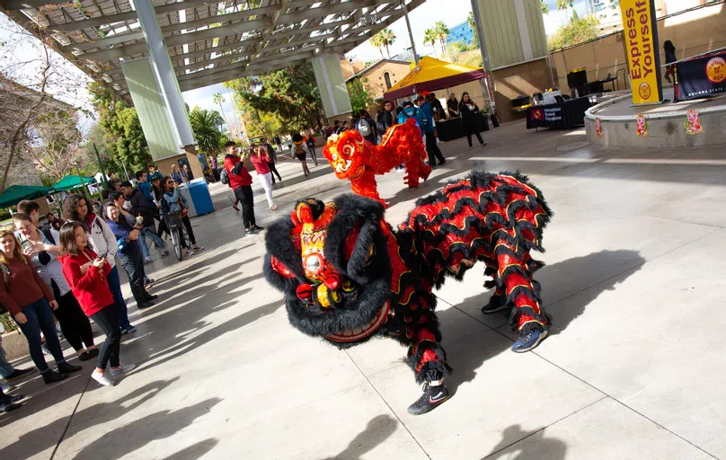 Group of people gather around performers in two-person Chinese dragon costumes. 