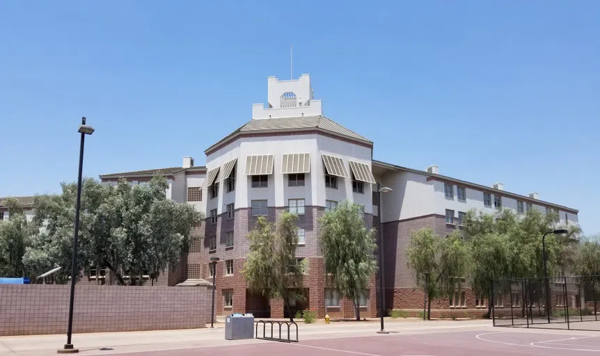 A basketball court and bike rack are in front of a five-story cinderblock and stucco building. 