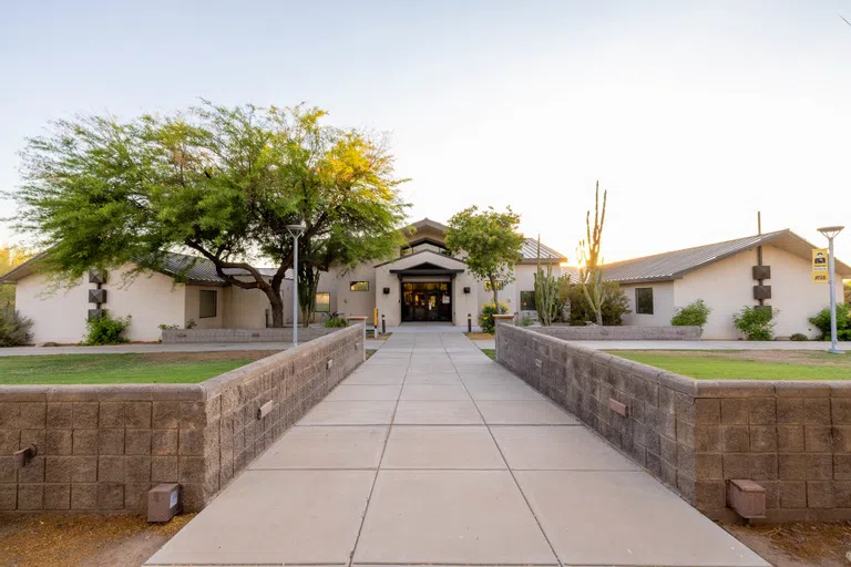 Three-foot wall-lined walkway leads up to a white one-story building 