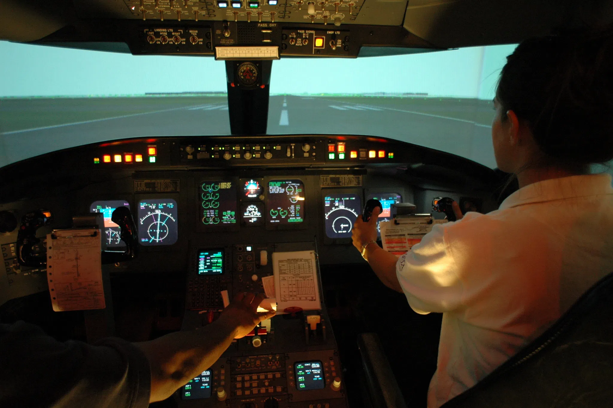 Man and Woman sit at controls of an airplane cockpit simulator.