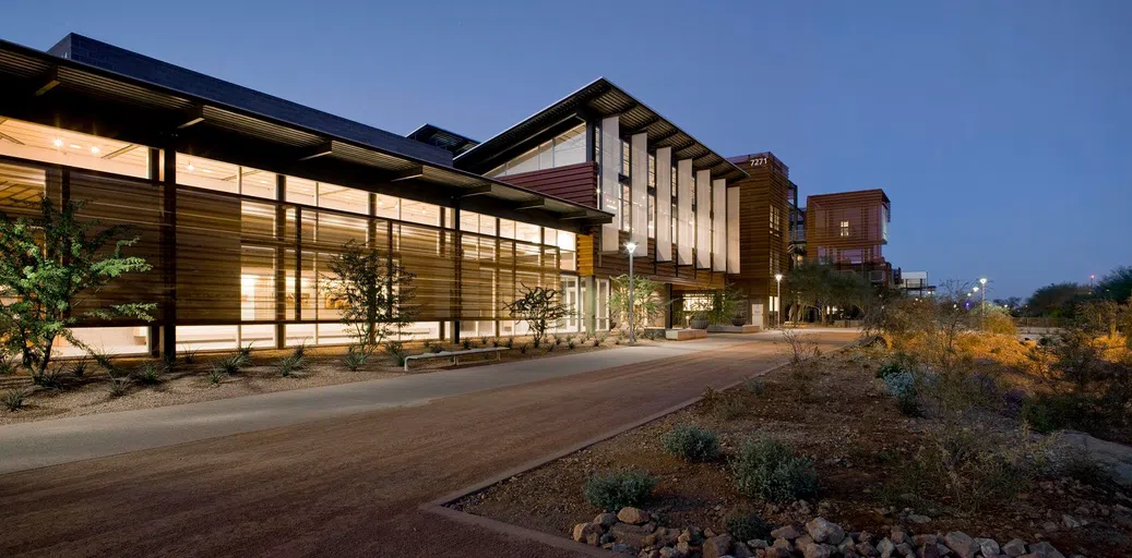 A gravel and concrete walkway leads to a two-story metal-clad building at dusk.