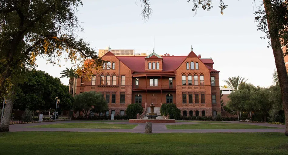 Grassy quad and fountain in front of Old Main at sunrise.