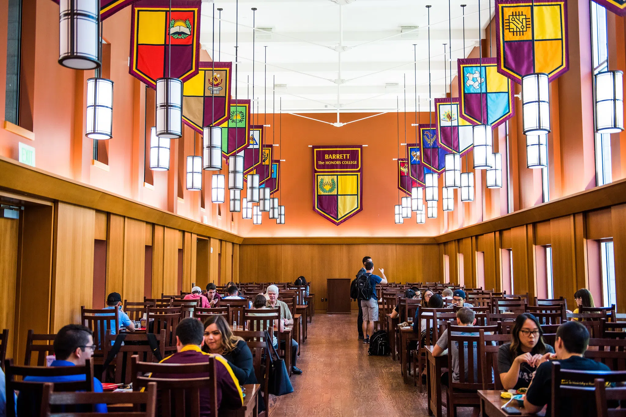 Students and faculty eating inside refectory of Barrett dining hall. Flags of each of ASU's colleges hang from the ceiling.