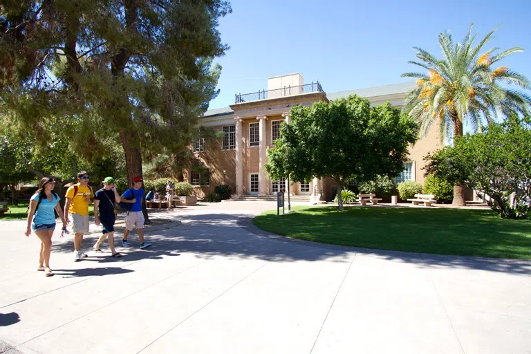 Four students walk by a two-story building with columns in front of the entrance.