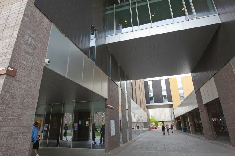 A walkway between two buildings. To the left is glass-walled first floor entrance to building.