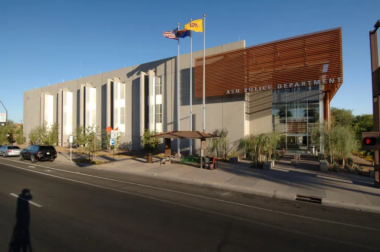 A bus stop and federal, state and ASU flag poles sit in front of the two-story concrete building with a copper mesh screen structure on it that says ASU Police Department.