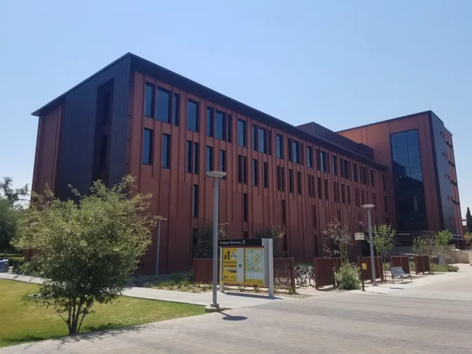 A walkway and campus map sign are in front of a multi-story red brick building. 