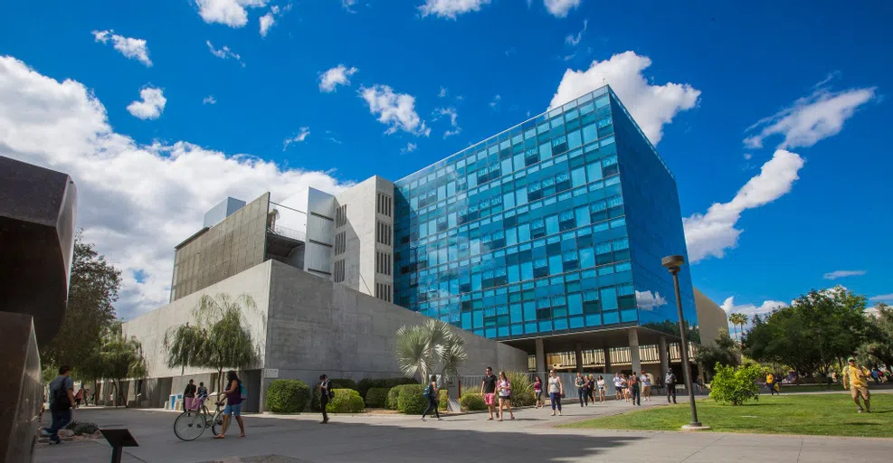 Students walk by a concrete and blue glass multi-story building.