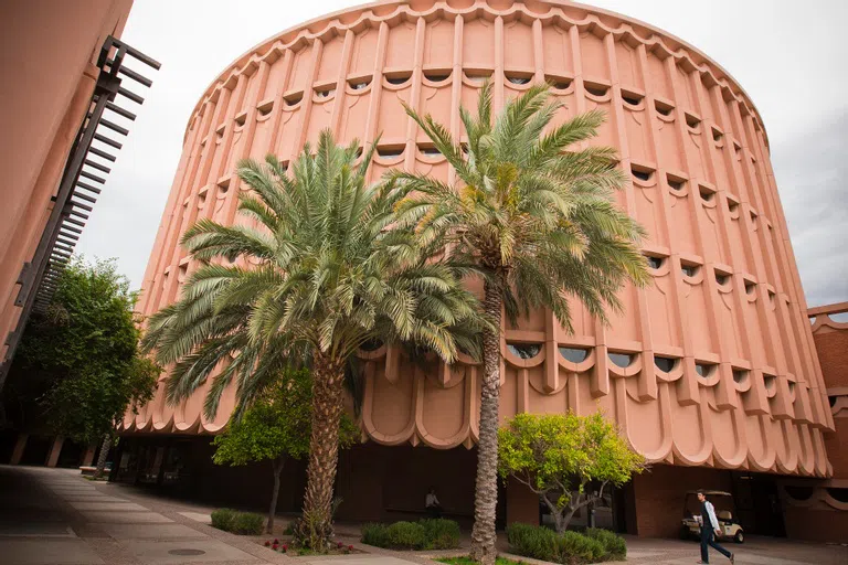 A person walks in front of a five-story sandstone-colored circular building with scalloped windows.