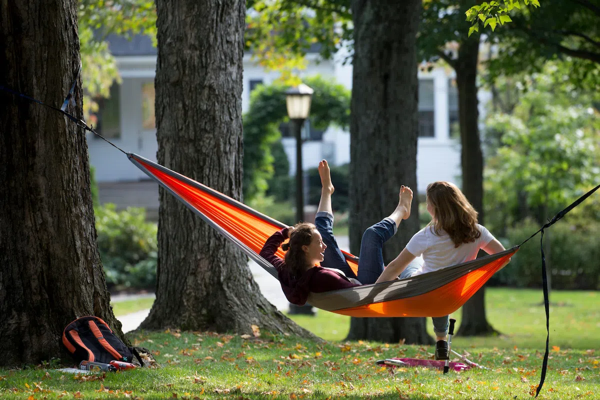 Two students relax in a hammock strung between two trees in the Quad