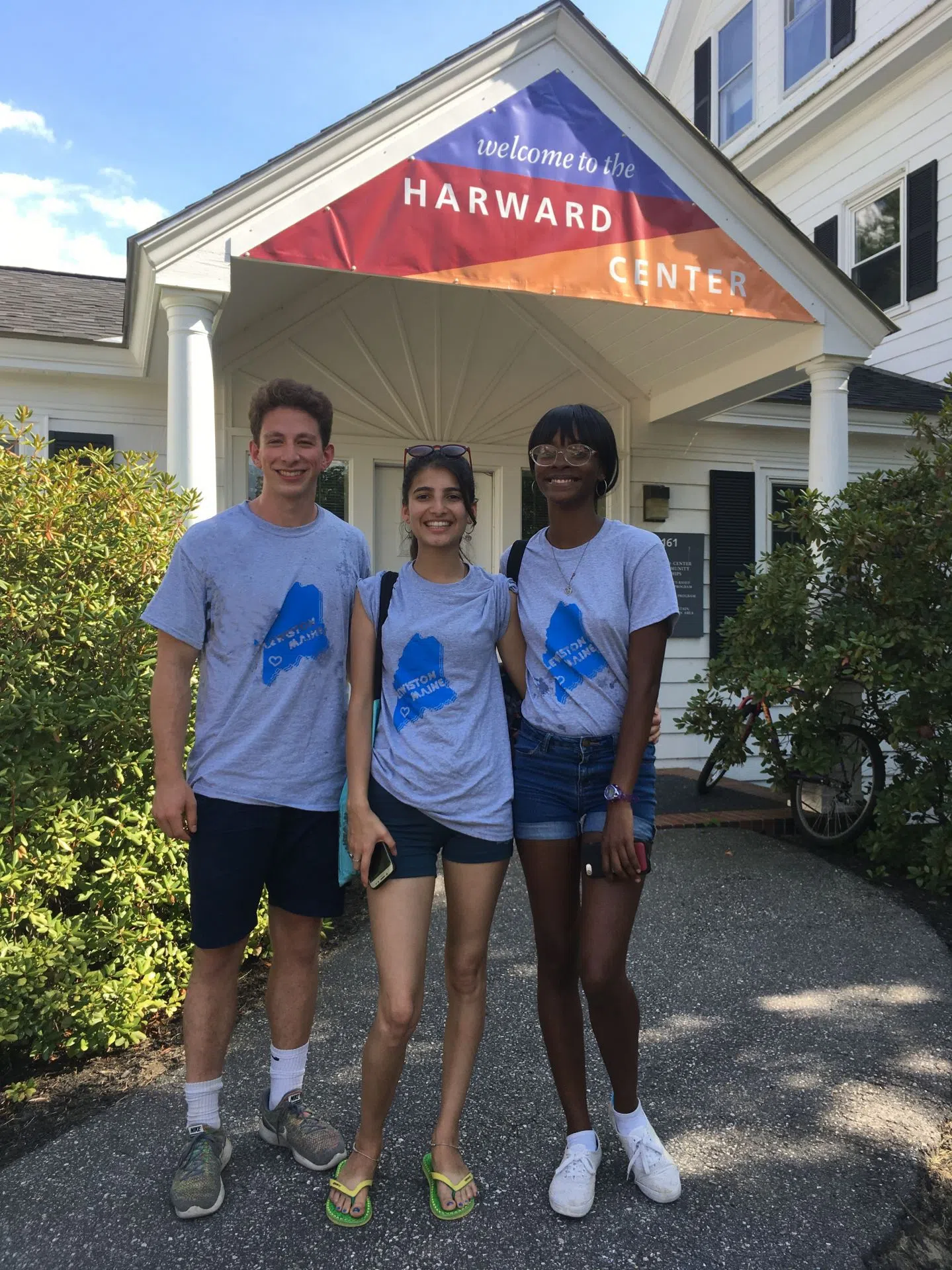 Three students stand outside a white building whose banner reads 'Welcome to the Harward Center'