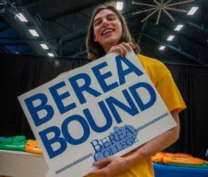 Smiling male student in yellow shirt holds large sign with text on it. Text reads "Berea Bound"