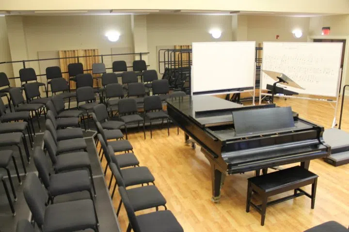 An interior photo of a rehearsal hall with piano in the center and seating surrounding it. 