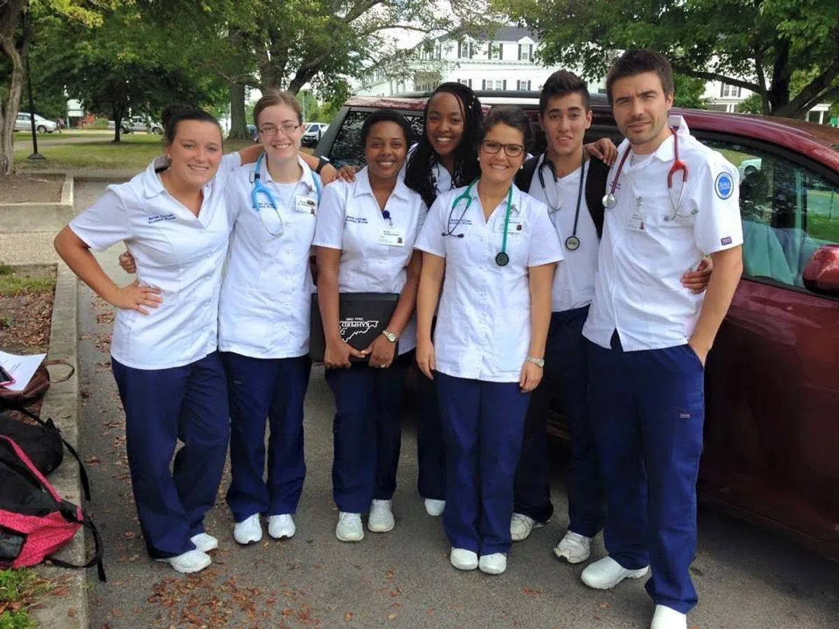 A group of nursing students wearing scrubs smile. 