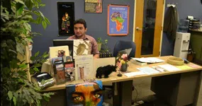 Student sits behind a welcome desk in the CIE. Maps and cultural artifacts adorn the walls.