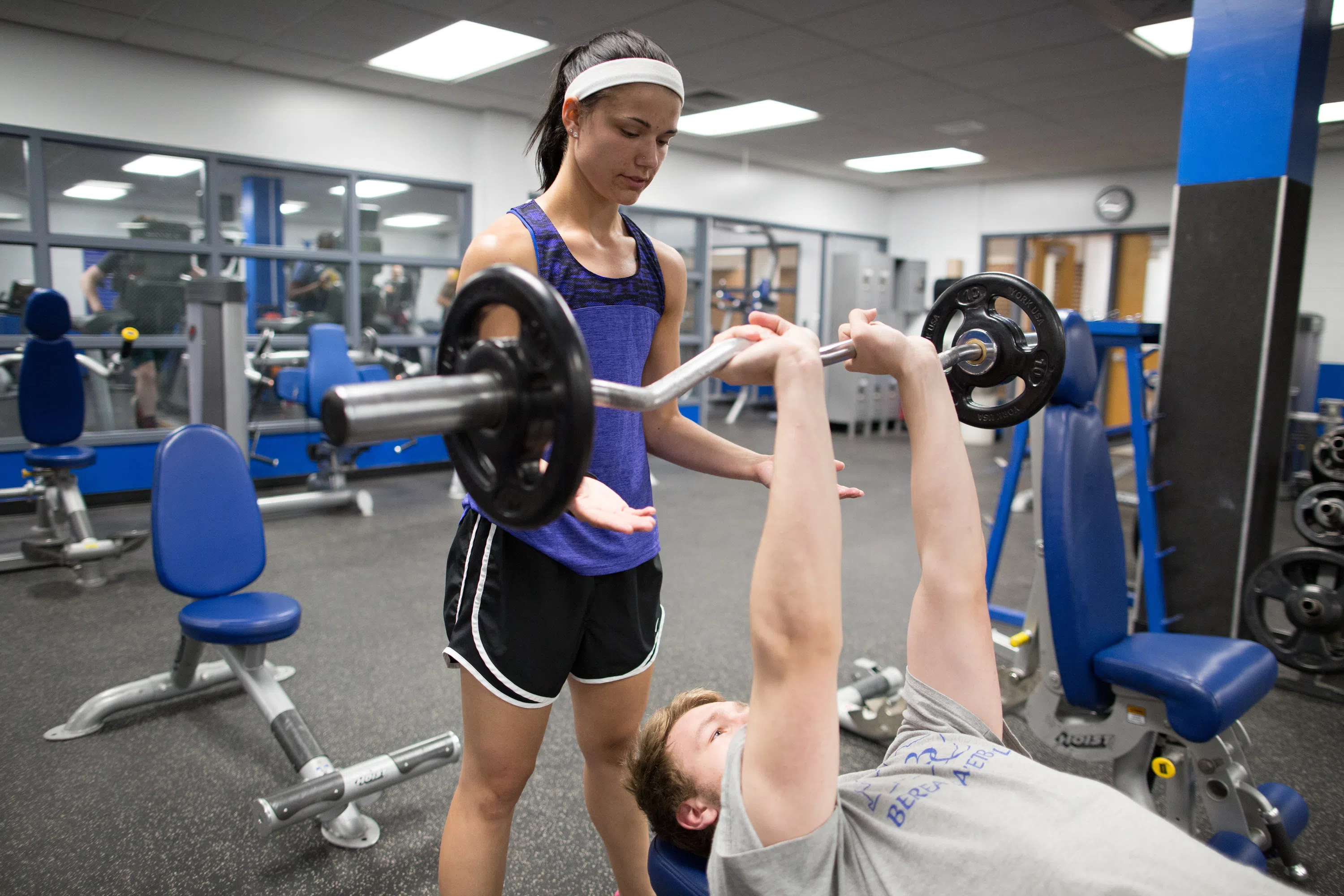 Female student helps "spot" a male student who is bench pressing weights..