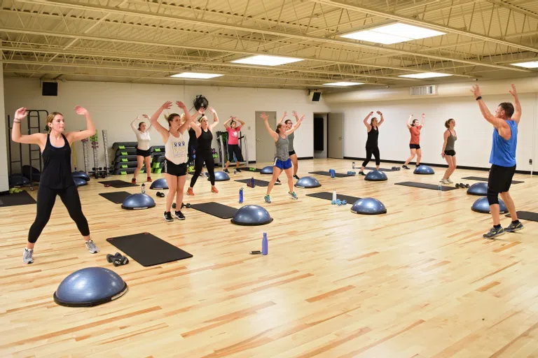 a group of students perform jumping jacks in a workout studio