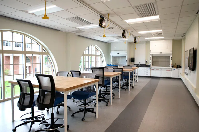 several empty tables with chairs surrounding them, with two hoods in the background and two large half-circle windows to the side