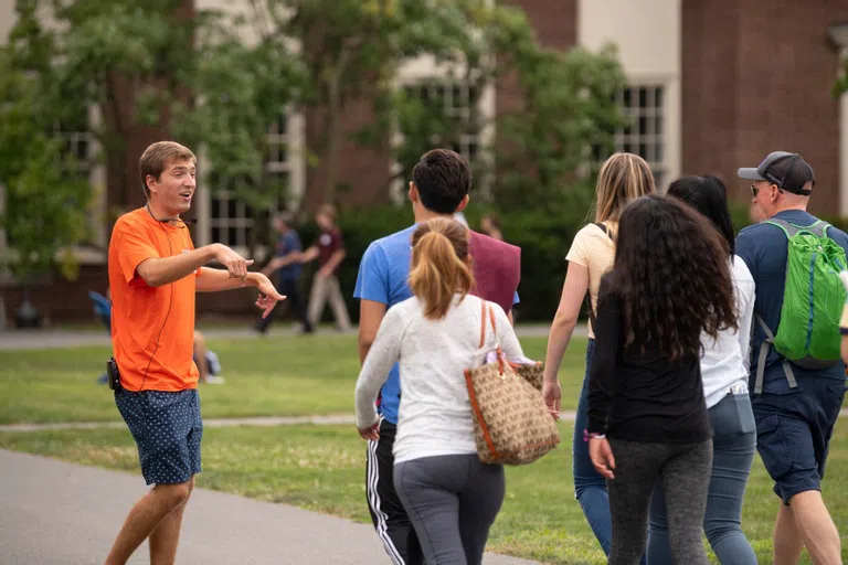 male tour guide walks backwards while talking with tour group on quad