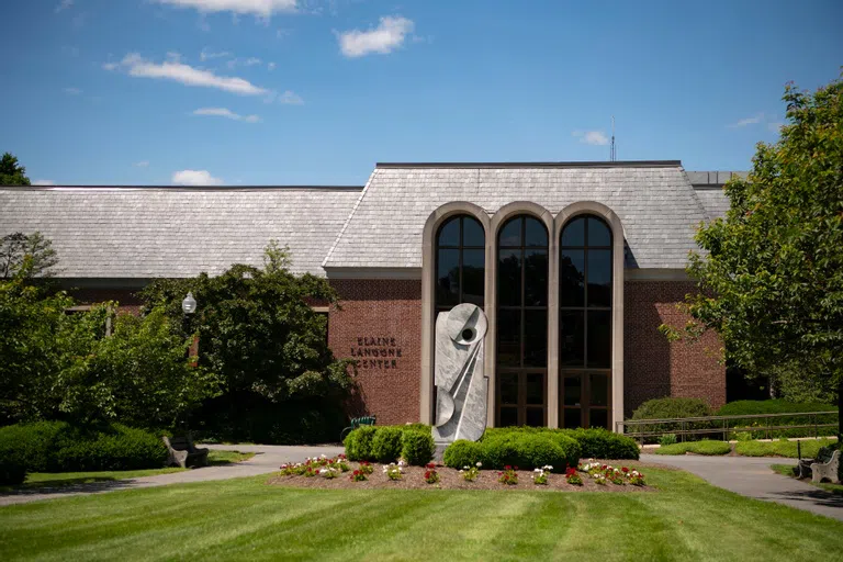 the rear entrance of Elaine Langone Center, with a statue in the foreground, the building behind, and lined by trees on either side