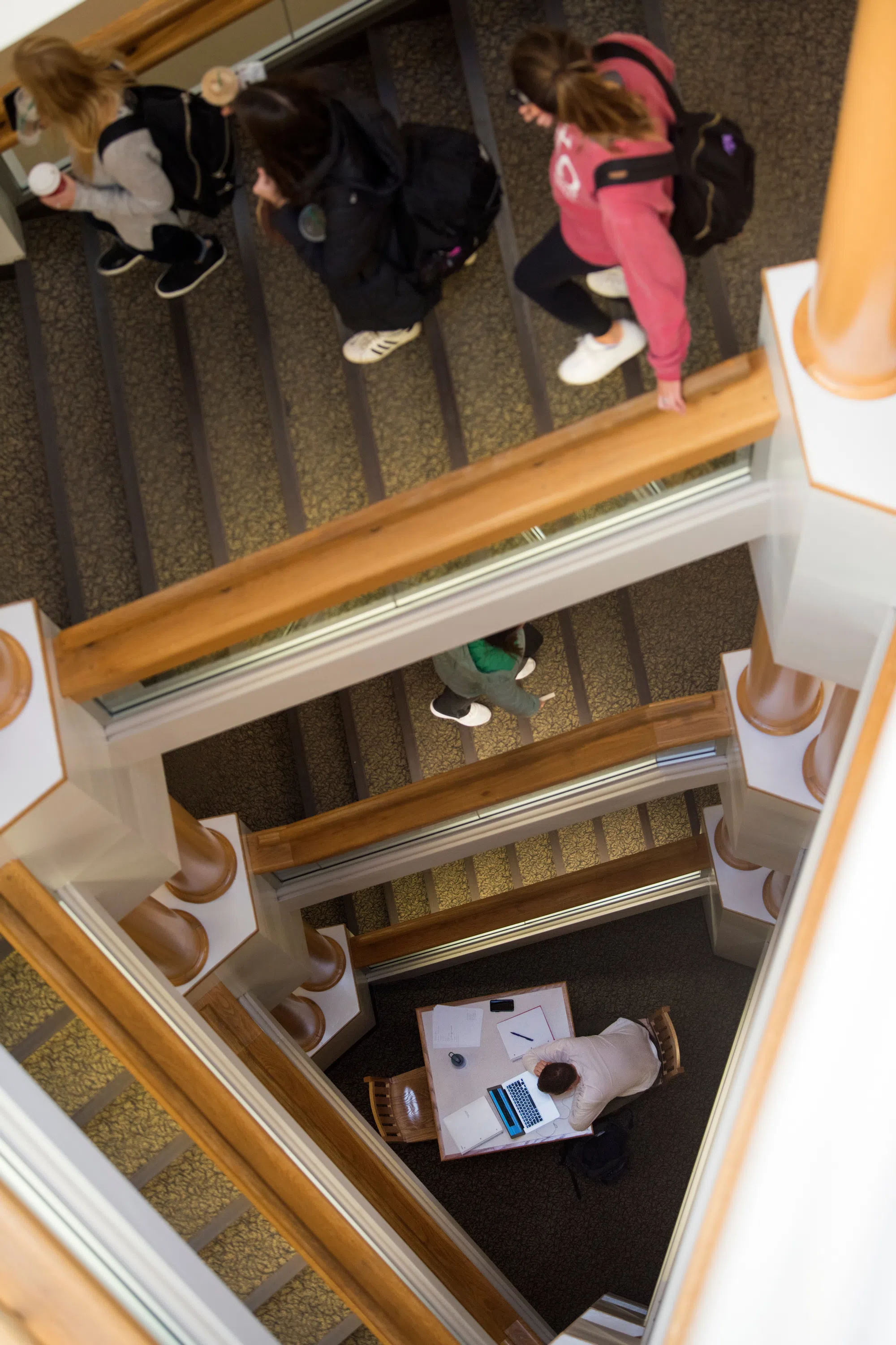 students walk staircase, with several stories visible, a student studying at a table at the bottom of the staircase