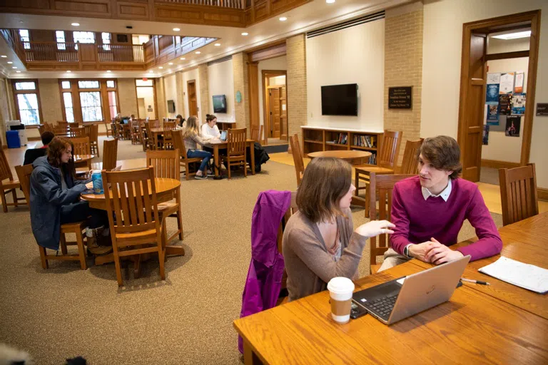 students study in groups around several tables in a large room