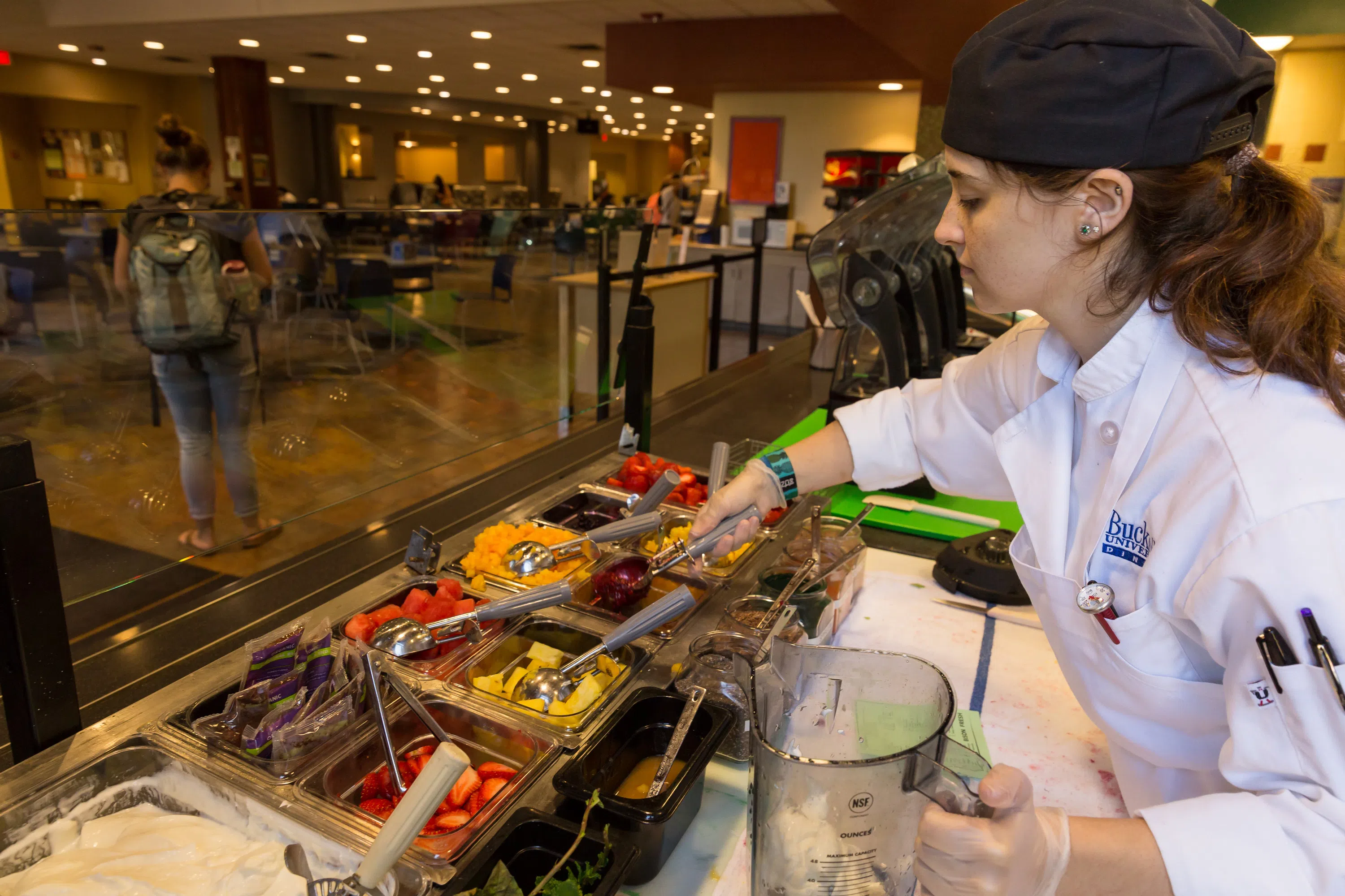 a female food service worker fills fresh fruit in a bowl at her station