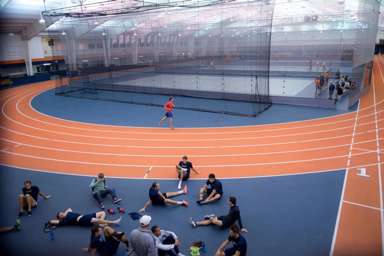 a student runs around a track with a group of students sitting off to the side of the track