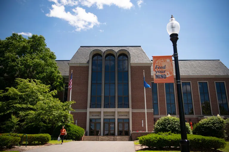 front entrance of Elaine Langone Center at ground-level, a student carrying a bag walking away from the building