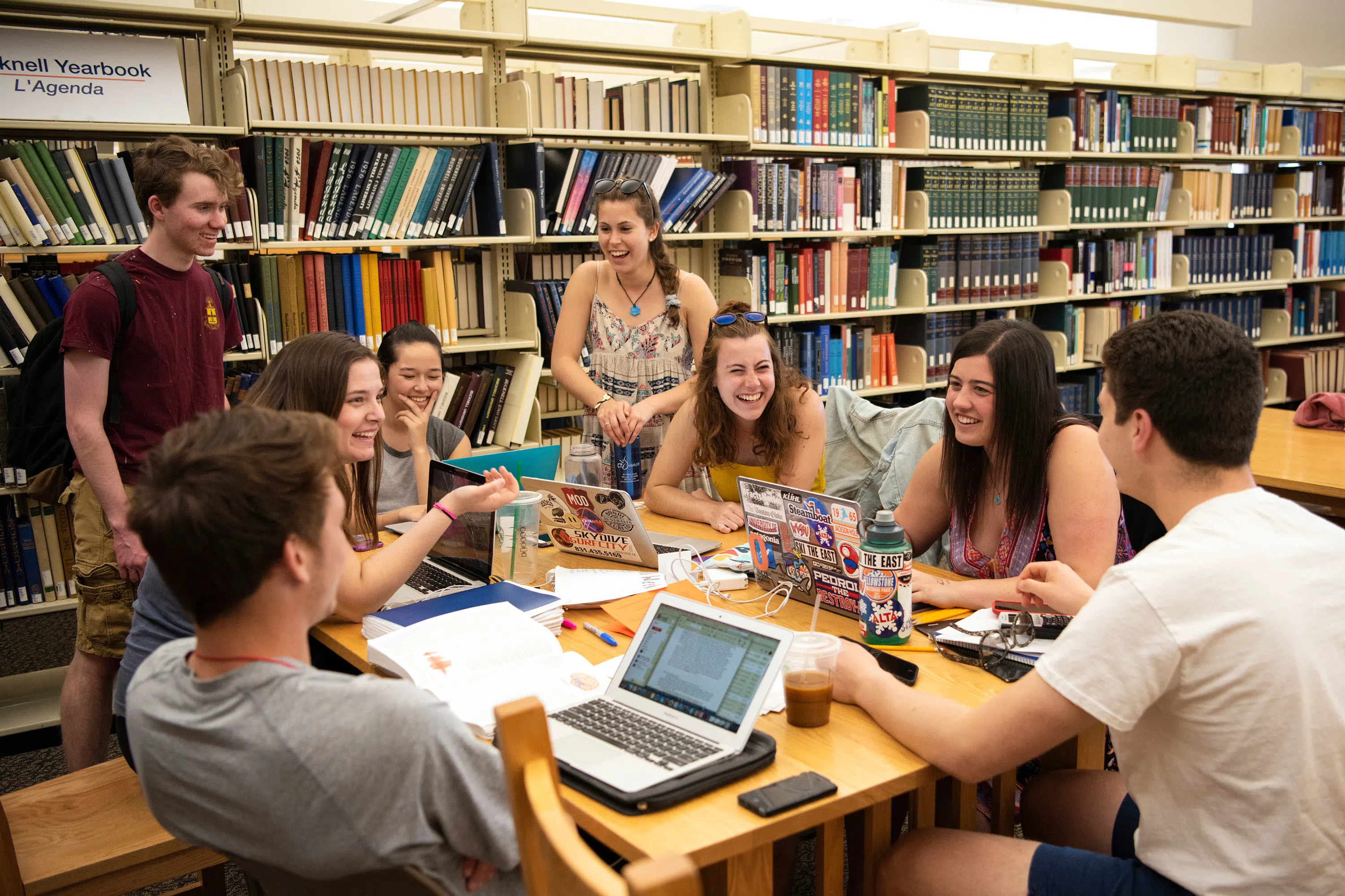 8 students work together around a table in Bertrand Library, books behind them