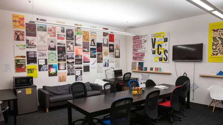 A small room with colorful posters lined up on the wall and a black couch, black table, and black chairs. 