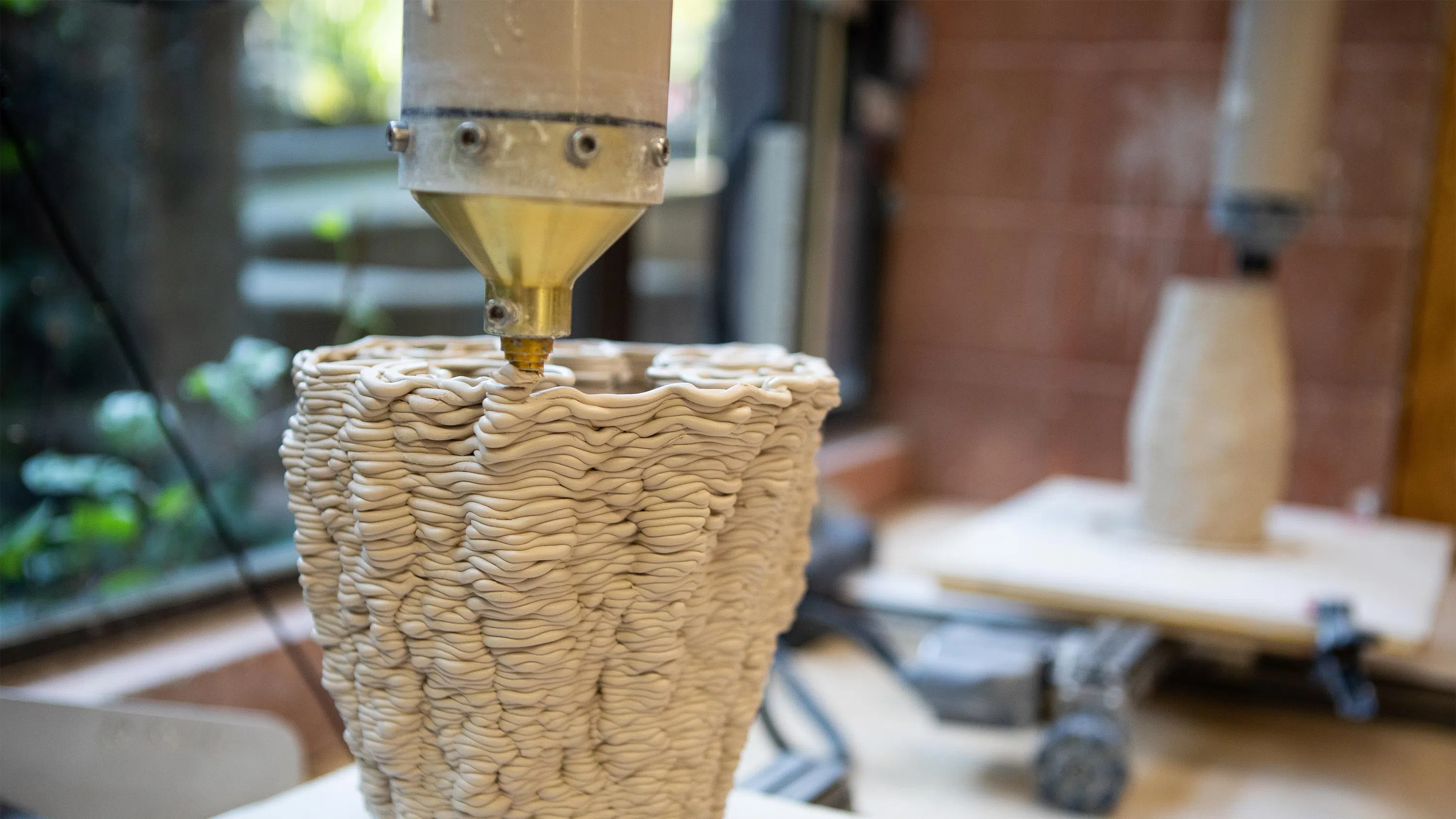 A close-up of a work-in-progress 3D printed clay vessel being extruded.
