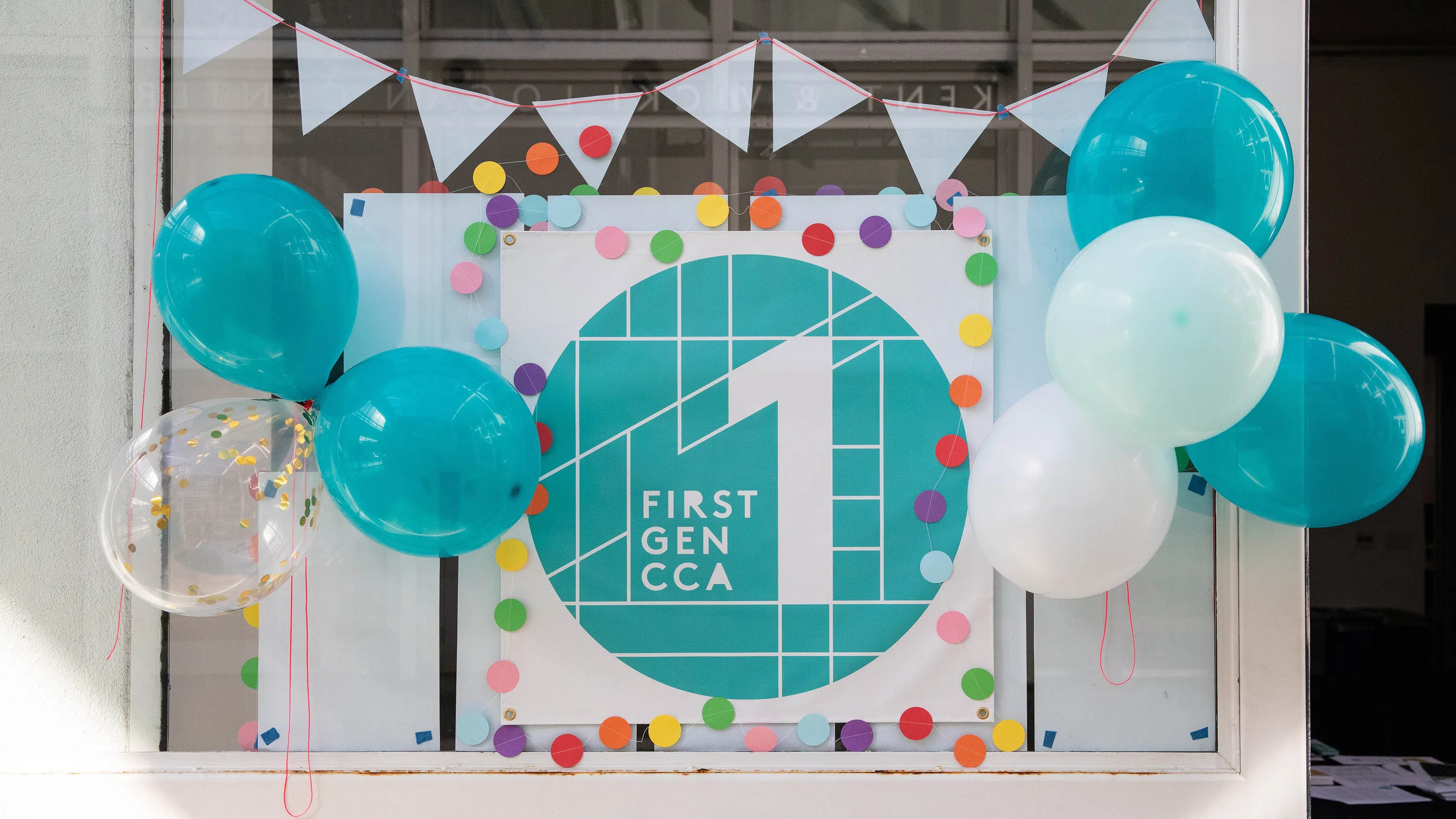 Balloons, flags, and colorful dots surround a teal-and-white poster that reads “First Gen CCA 1.”
