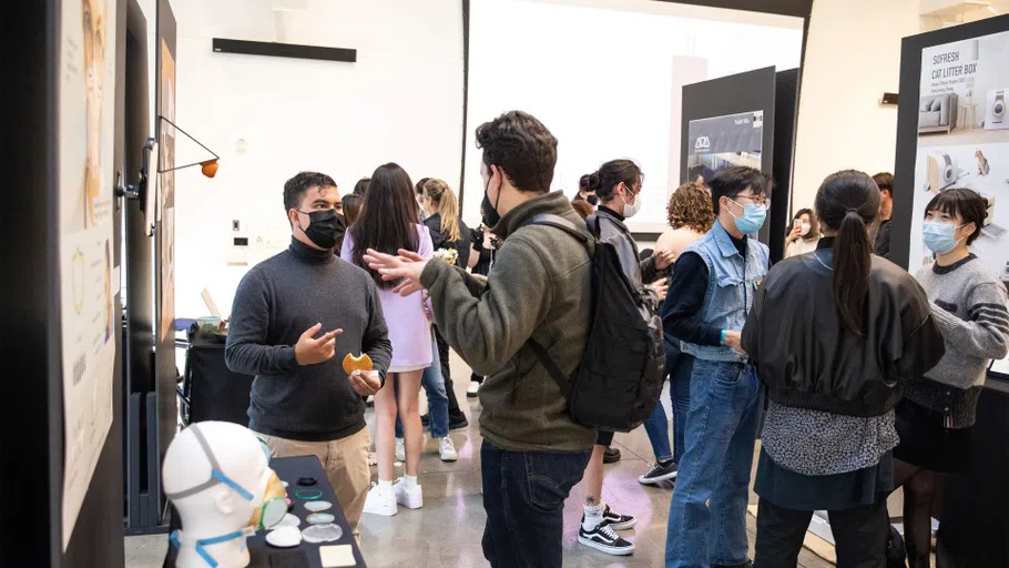 Students talk to the public, presenting concepts and prototypes for final projects in booths draped with black cloth.