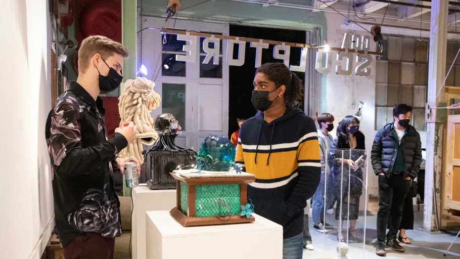 Two students talk in front of a box-like sculpture on a pedestal.