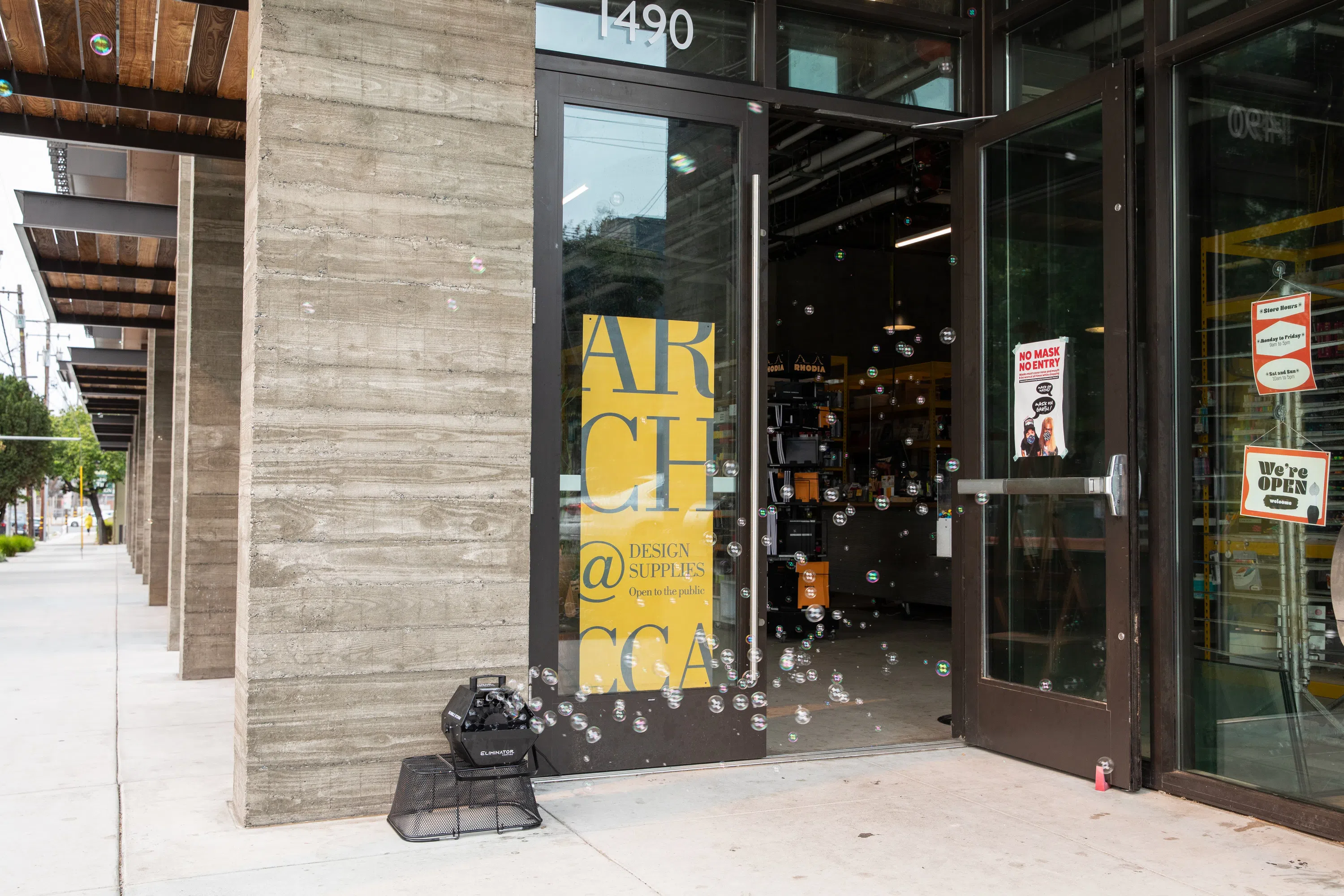 The exterior of ARCH Art Supplies in the ground floor of Blattner Hall, with bright yellow signage and a bubble machine. 