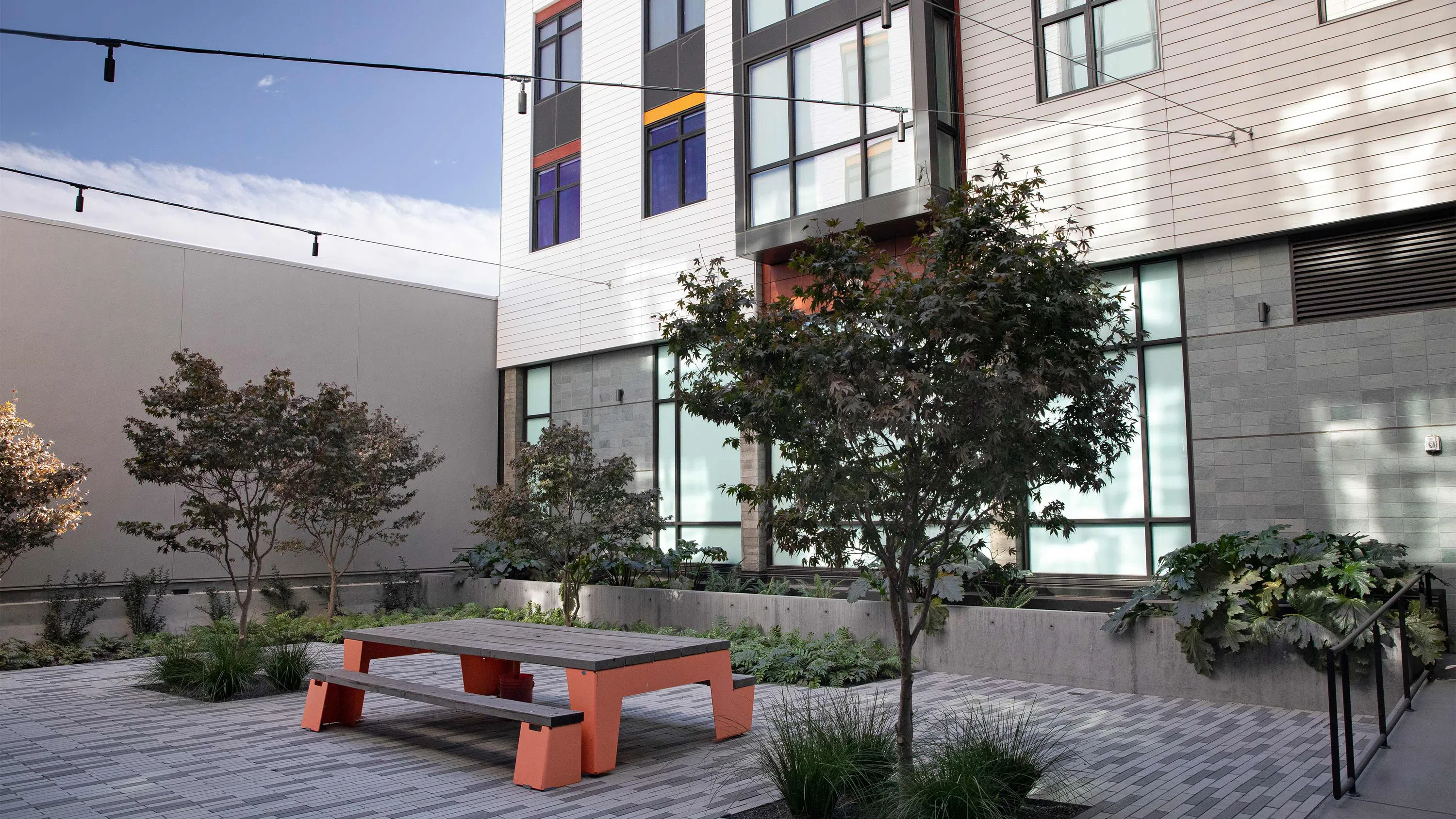 An exterior view of the interior courtyard that includes orange-and-wood tables and benches and greenery.